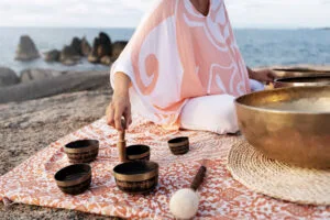 Femme faisant de la sonothérapie près de la mer, avec des bols tibétains. Equilibrer ses chakras